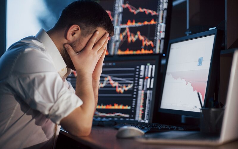 Stressed trader monitoring market loss on multiple computer screens