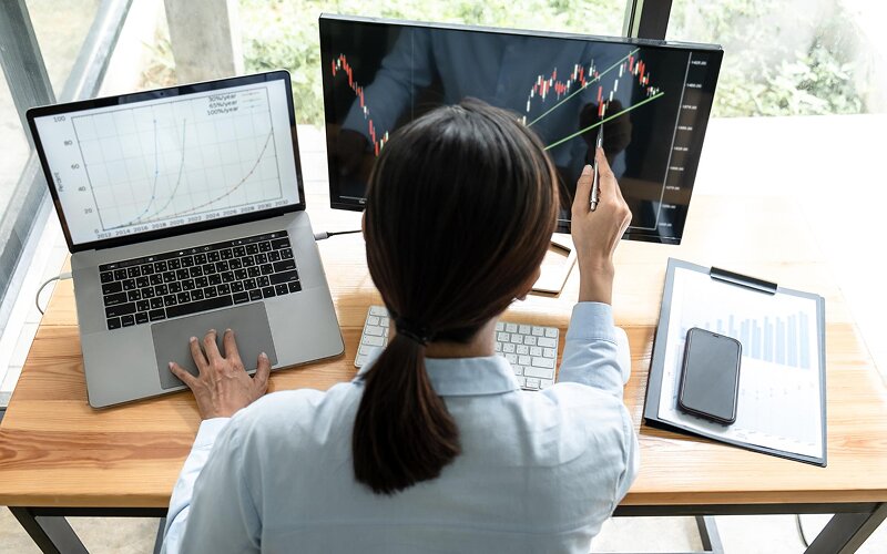 Trader analyzing growth charts on a laptop and monitor